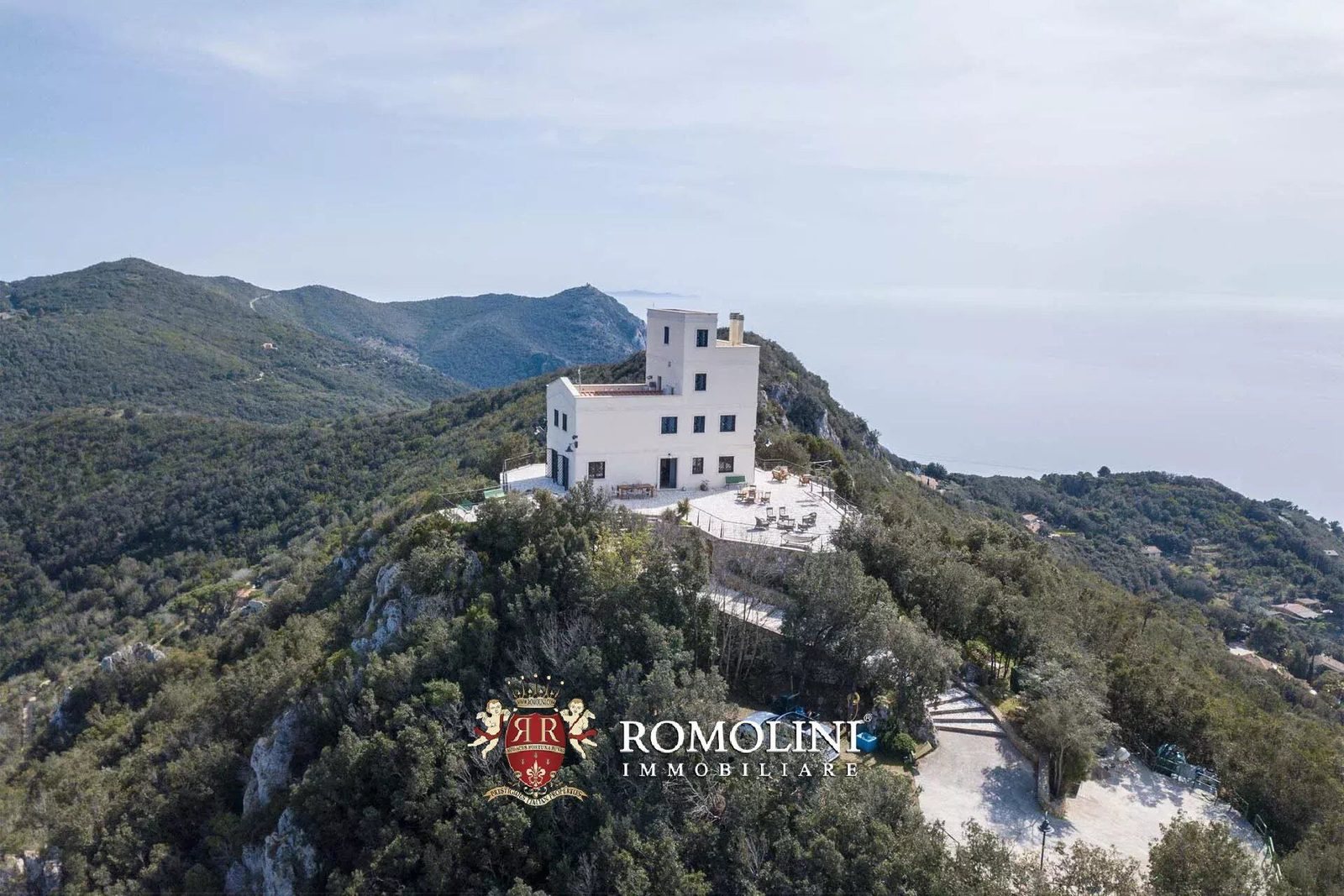 Aerial view of the white lighthouse villa and its paved terraces on a wooded ridge of Monte Argentario above the sea