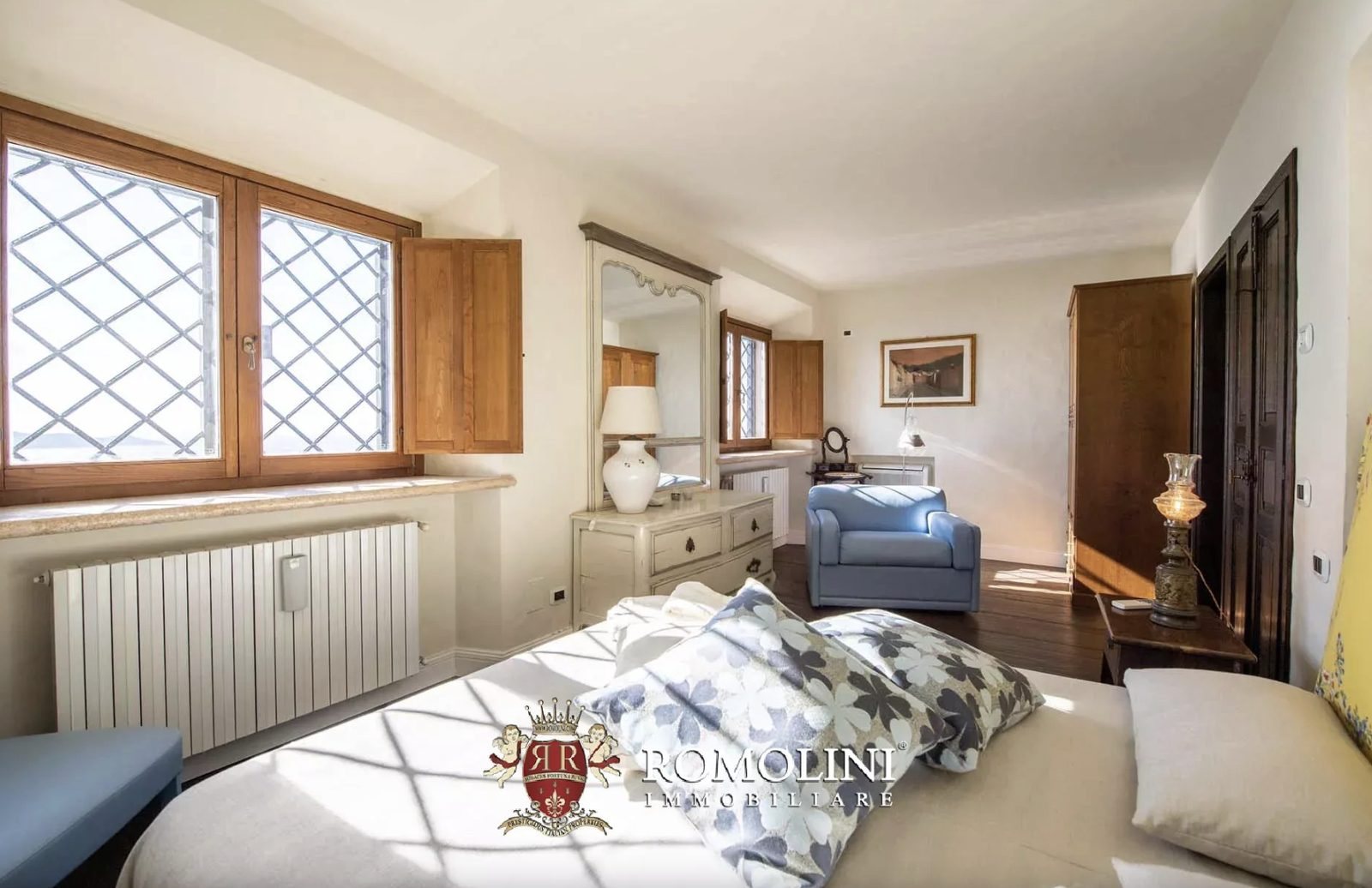 Bright bedroom with leaded windows, painted dresser, and blue armchair in the Monte Argentario lighthouse villa