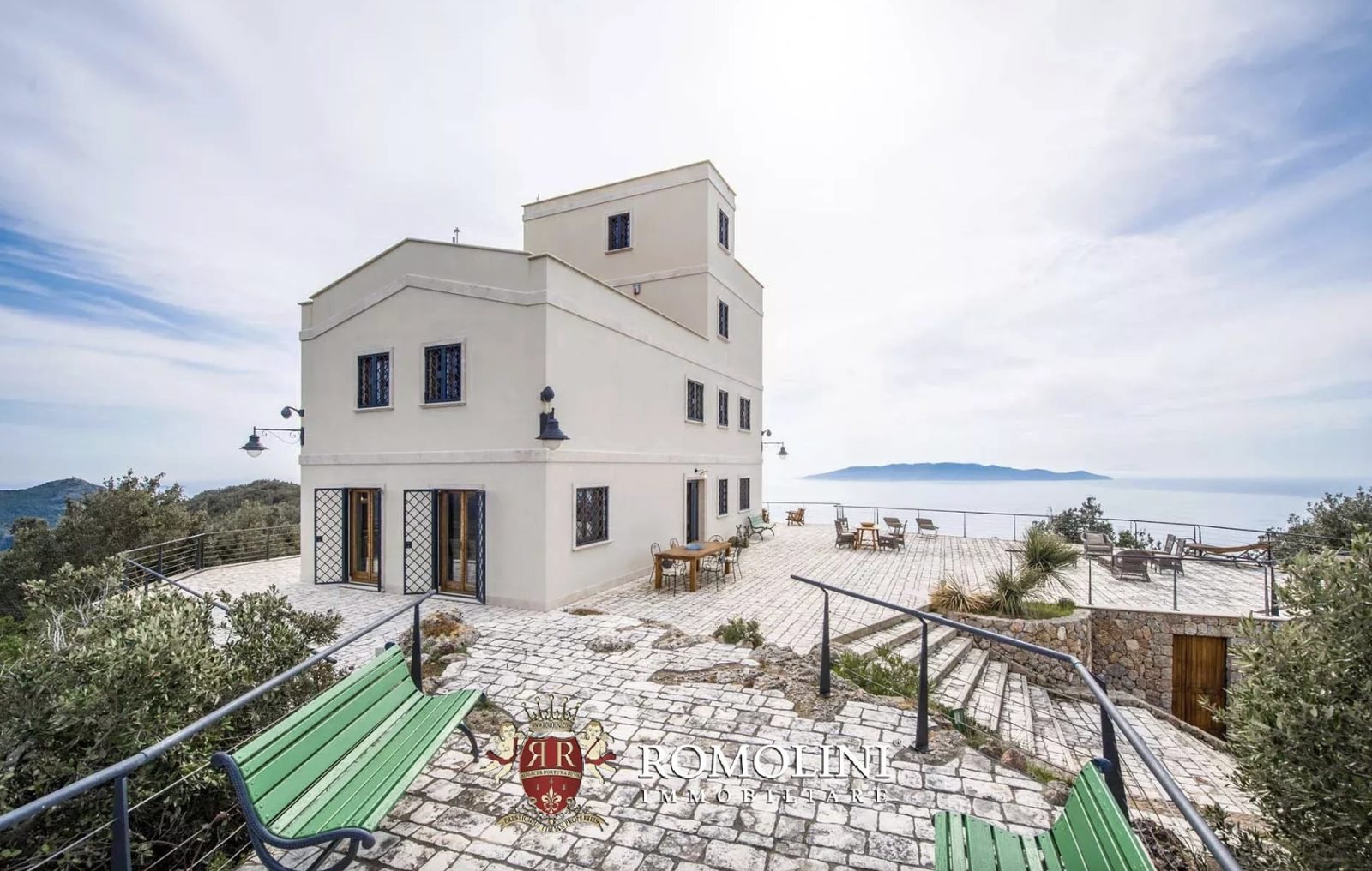 Stone-paved terrace and outdoor dining area around the white lighthouse tower with Giglio Island visible across the sea